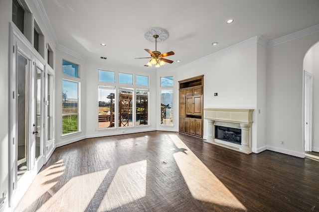 unfurnished living room with dark wood-type flooring, a fireplace with raised hearth, arched walkways, crown molding, and baseboards