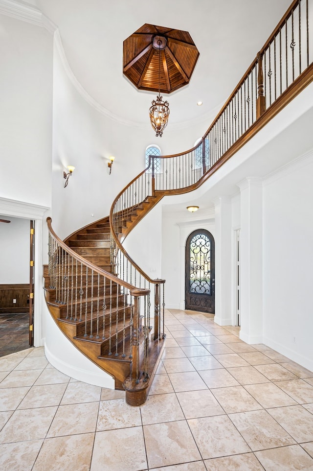 foyer entrance featuring tile patterned floors, crown molding, a chandelier, and a high ceiling