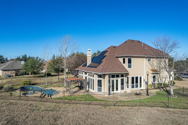 rear view of house featuring roof mounted solar panels, a fenced backyard, a patio area, and a chimney