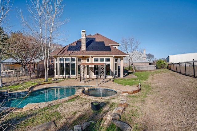 back of house with a fenced backyard, a fenced in pool, roof mounted solar panels, a chimney, and a patio area
