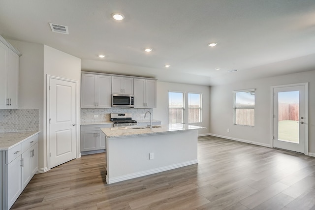 kitchen featuring light stone countertops, stainless steel appliances, a center island with sink, and sink