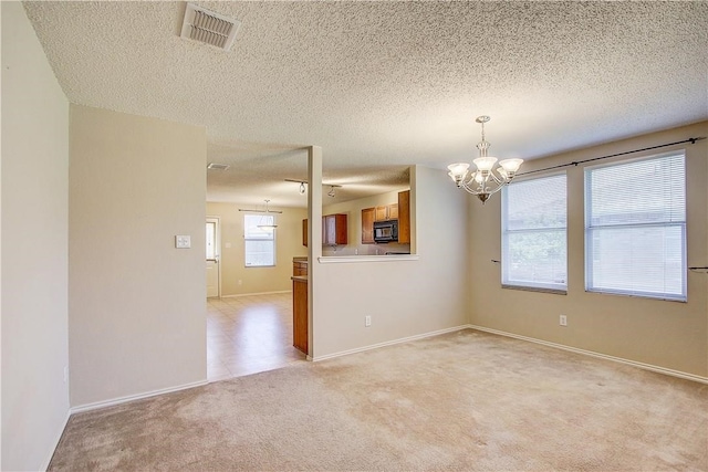 spare room featuring light carpet, a textured ceiling, and an inviting chandelier