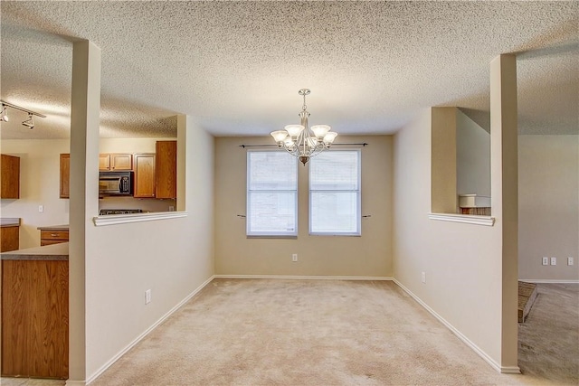 unfurnished dining area featuring a textured ceiling, an inviting chandelier, light carpet, and track lighting