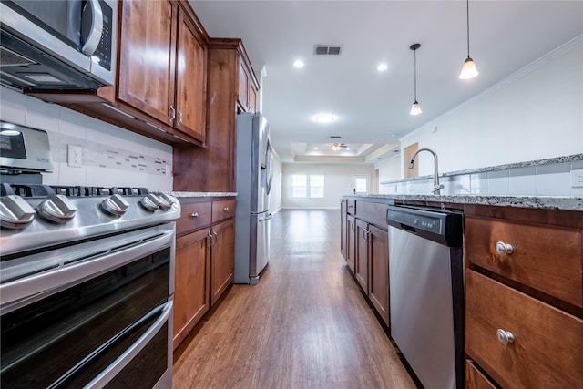 kitchen featuring appliances with stainless steel finishes, decorative light fixtures, ornamental molding, light stone counters, and a tray ceiling