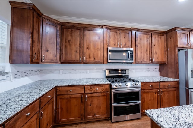 kitchen with light stone countertops, stainless steel appliances, backsplash, ornamental molding, and light wood-type flooring