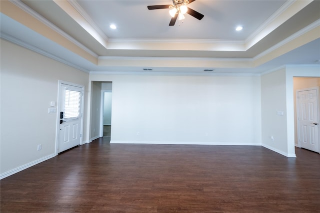 empty room featuring dark wood-type flooring, a tray ceiling, and crown molding