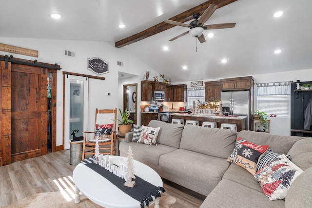 living room featuring lofted ceiling with beams, a barn door, light hardwood / wood-style floors, and ceiling fan