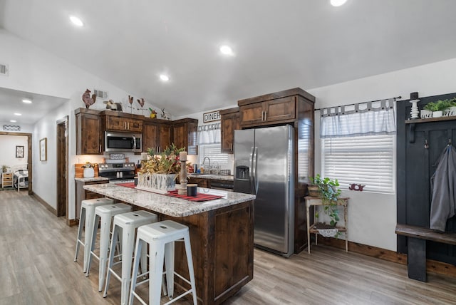 kitchen with dark brown cabinetry, lofted ceiling, a breakfast bar area, a kitchen island, and appliances with stainless steel finishes