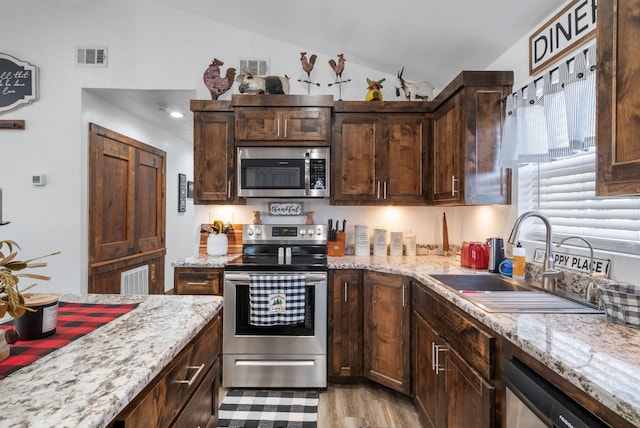 kitchen with light stone countertops, appliances with stainless steel finishes, dark brown cabinetry, and sink