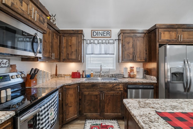 kitchen with appliances with stainless steel finishes, light wood-type flooring, light stone counters, dark brown cabinets, and sink