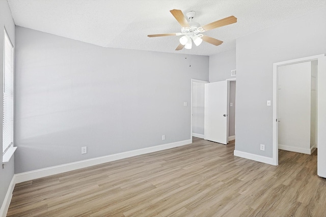 unfurnished bedroom featuring a textured ceiling, a walk in closet, a closet, and ceiling fan