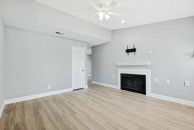 unfurnished living room with a tiled fireplace, a textured ceiling, light hardwood / wood-style flooring, and ceiling fan