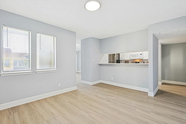 unfurnished living room featuring a textured ceiling, light wood-type flooring, and a healthy amount of sunlight