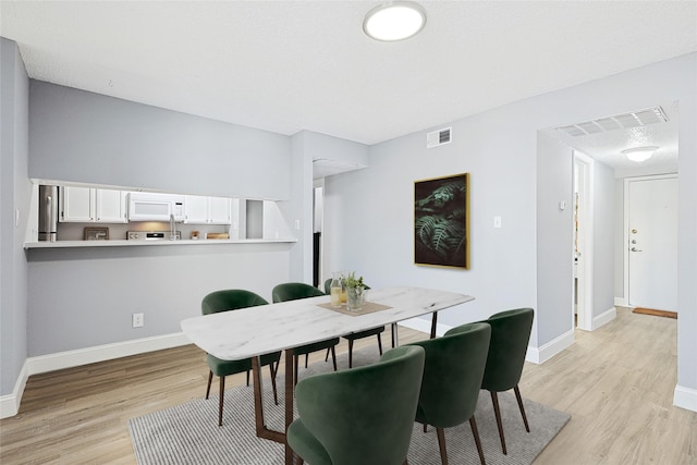 dining space with a textured ceiling and light hardwood / wood-style flooring