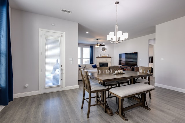 dining space featuring hardwood / wood-style flooring, a stone fireplace, and ceiling fan with notable chandelier