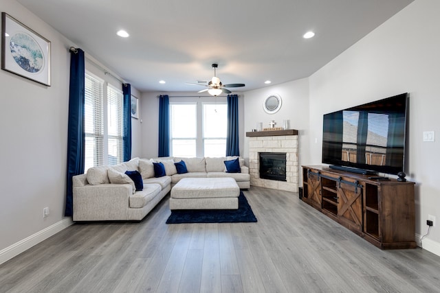 living room featuring a fireplace, ceiling fan, and light wood-type flooring