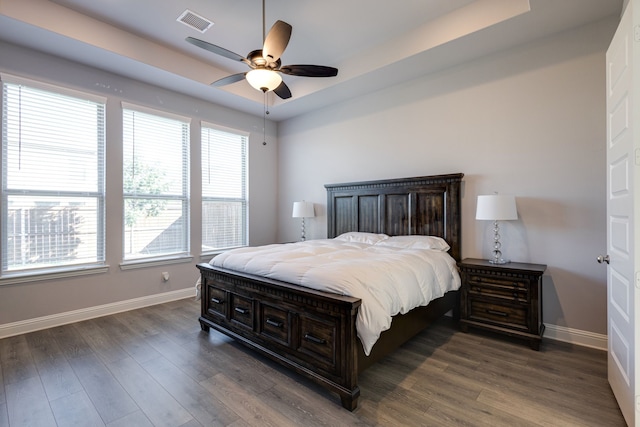 bedroom with dark wood-type flooring, ceiling fan, and a tray ceiling