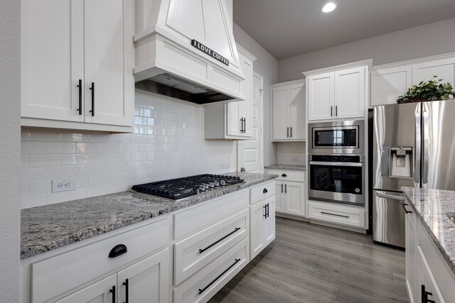 kitchen featuring premium range hood, white cabinetry, stainless steel appliances, and light stone countertops