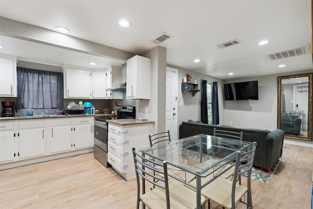 kitchen featuring stainless steel electric range, light hardwood / wood-style floors, dark stone countertops, and white cabinetry