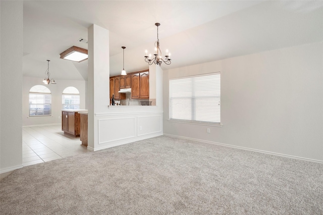 interior space featuring kitchen peninsula, light colored carpet, an inviting chandelier, hanging light fixtures, and lofted ceiling