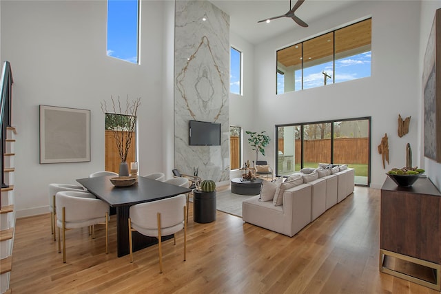 living room featuring ceiling fan, light wood-type flooring, a high ceiling, and a premium fireplace