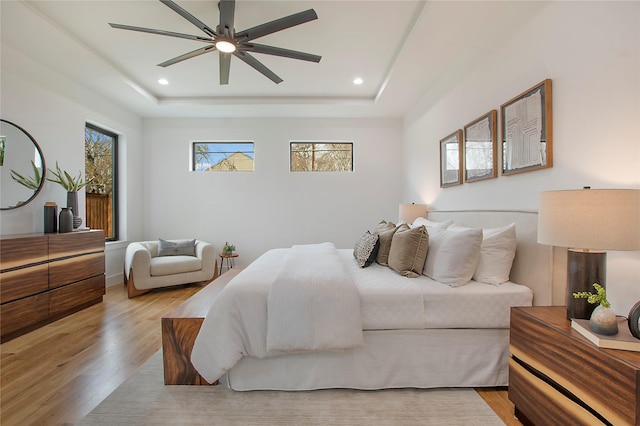 bedroom featuring ceiling fan, a raised ceiling, and light hardwood / wood-style flooring