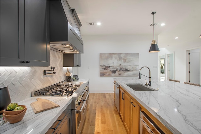 kitchen featuring appliances with stainless steel finishes, light wood-type flooring, light stone counters, sink, and pendant lighting