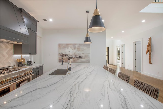 kitchen featuring light stone countertops, sink, range with two ovens, decorative light fixtures, and decorative backsplash