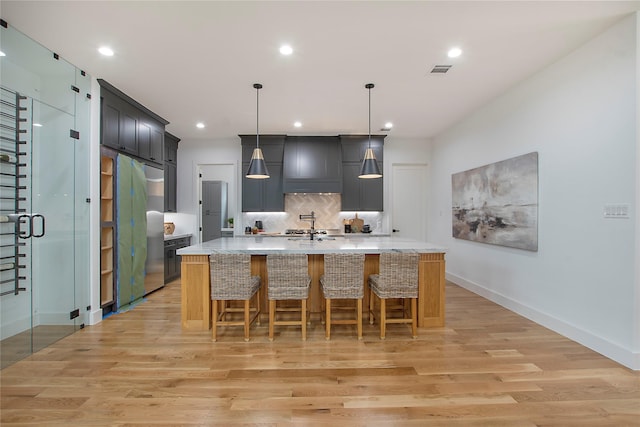 kitchen featuring a center island with sink, decorative light fixtures, stainless steel fridge, and light wood-type flooring