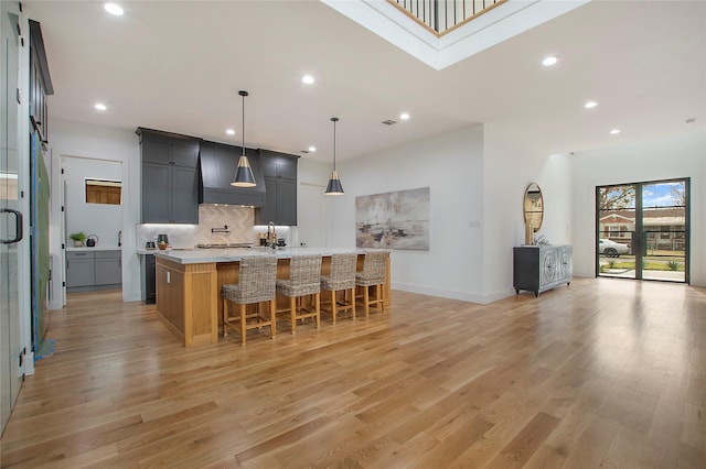 kitchen with a kitchen bar, light stone countertops, a large island with sink, pendant lighting, and light hardwood / wood-style flooring