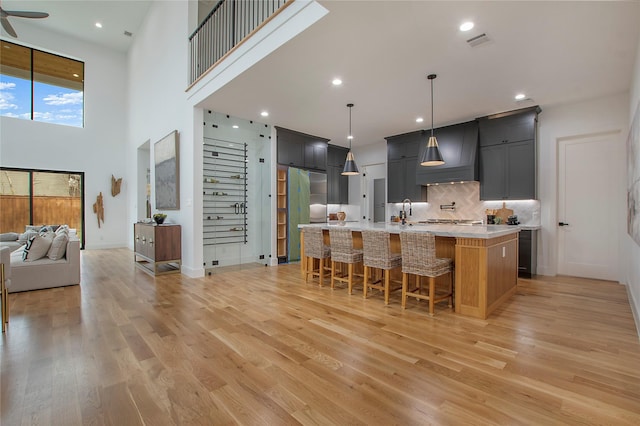 kitchen with custom range hood, light wood-type flooring, a center island with sink, and pendant lighting