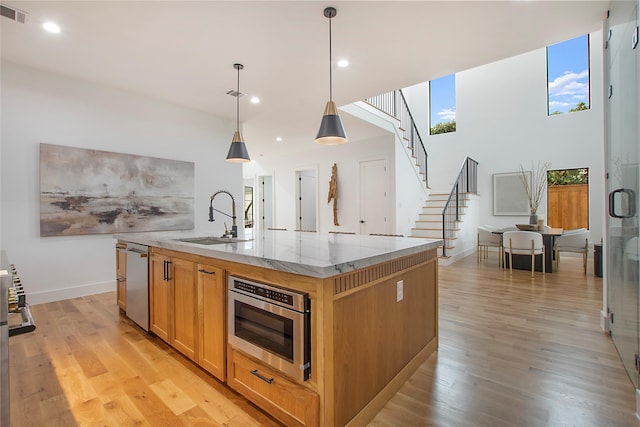 kitchen with light stone countertops, light wood-type flooring, sink, pendant lighting, and an island with sink