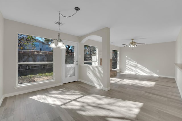 unfurnished dining area with ceiling fan with notable chandelier and light hardwood / wood-style floors