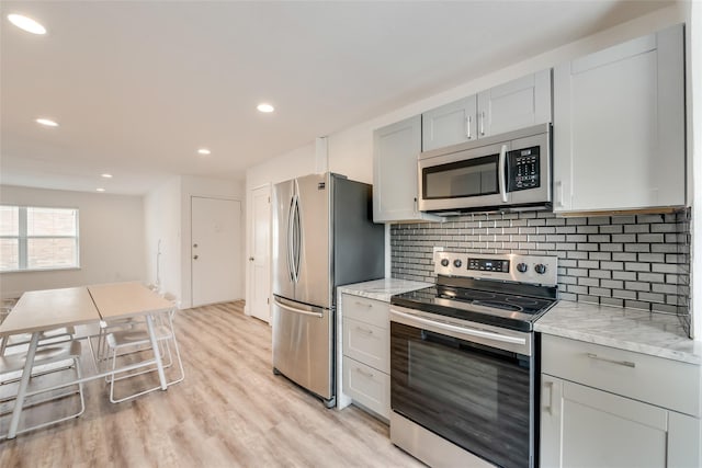 kitchen with light stone counters, appliances with stainless steel finishes, tasteful backsplash, and light hardwood / wood-style flooring