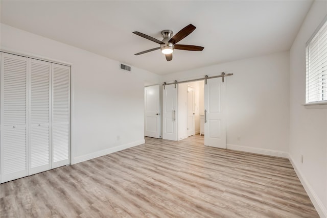 unfurnished bedroom featuring ceiling fan, a barn door, light hardwood / wood-style floors, and a closet