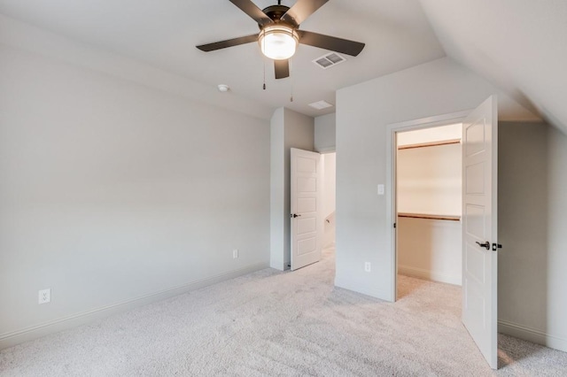 unfurnished bedroom featuring ceiling fan, a spacious closet, light colored carpet, vaulted ceiling, and a closet