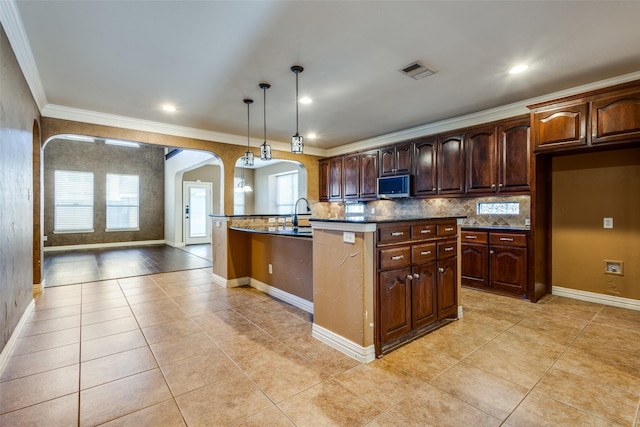 kitchen featuring light tile patterned flooring, ornamental molding, hanging light fixtures, and a kitchen island with sink