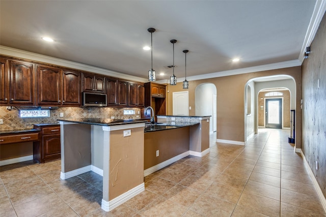 kitchen featuring a kitchen island with sink, crown molding, decorative light fixtures, decorative backsplash, and dark brown cabinets