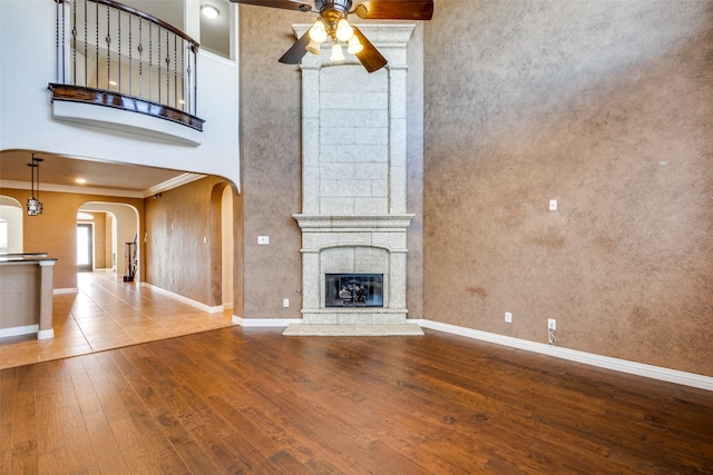 unfurnished living room featuring ceiling fan, a high ceiling, crown molding, hardwood / wood-style floors, and a fireplace