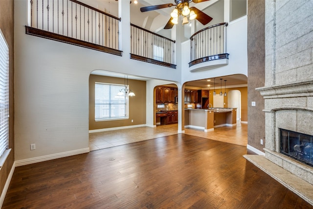 unfurnished living room with a high ceiling, crown molding, hardwood / wood-style floors, a fireplace, and ceiling fan with notable chandelier