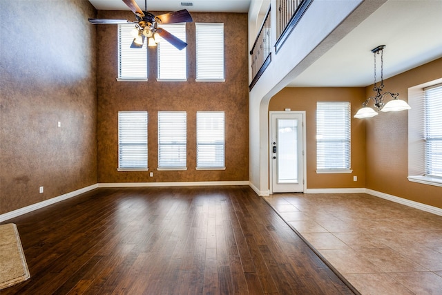 unfurnished living room with a high ceiling, ceiling fan with notable chandelier, and dark wood-type flooring