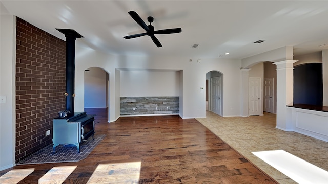 unfurnished living room featuring tile patterned floors, ceiling fan, a wood stove, and ornate columns