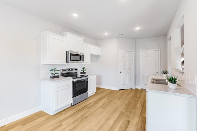 kitchen with white cabinets, appliances with stainless steel finishes, light hardwood / wood-style flooring, and sink