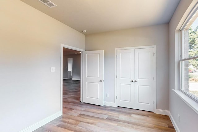 unfurnished bedroom featuring a closet, light hardwood / wood-style flooring, and multiple windows