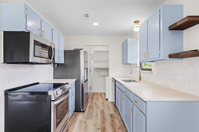 kitchen featuring sink, light hardwood / wood-style flooring, blue cabinetry, appliances with stainless steel finishes, and a textured ceiling