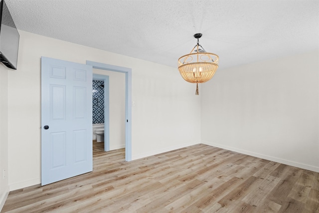 empty room featuring light hardwood / wood-style floors, a textured ceiling, and an inviting chandelier