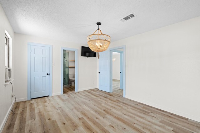 interior space featuring connected bathroom, light wood-type flooring, a textured ceiling, and an inviting chandelier