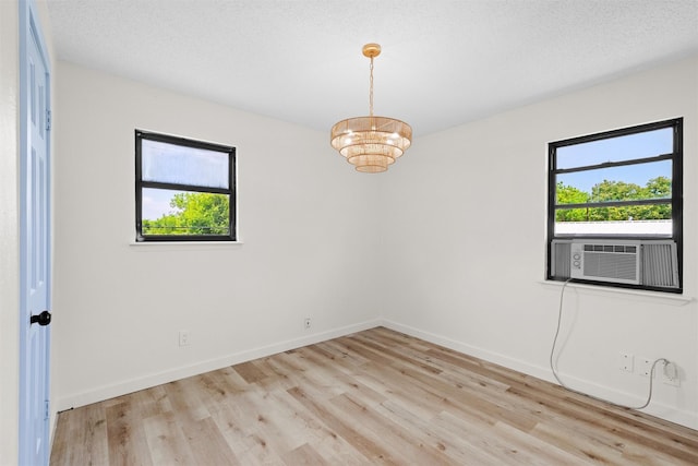 empty room featuring plenty of natural light, cooling unit, light wood-type flooring, and an inviting chandelier