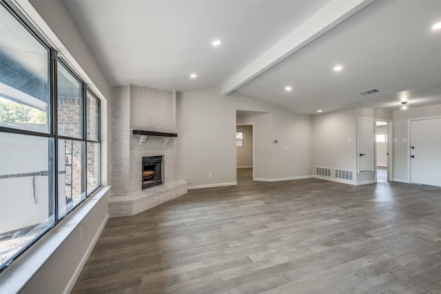 unfurnished living room with vaulted ceiling with beams, hardwood / wood-style floors, a healthy amount of sunlight, and a brick fireplace