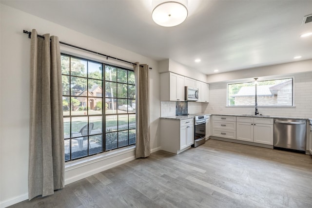 kitchen featuring stainless steel appliances, white cabinetry, plenty of natural light, and light hardwood / wood-style flooring